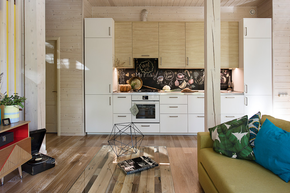 Идея дизайна: кухня-гостиная в современном стиле с плоскими фасадами, черным фартуком, белой техникой и паркетным полом среднего тона без острова