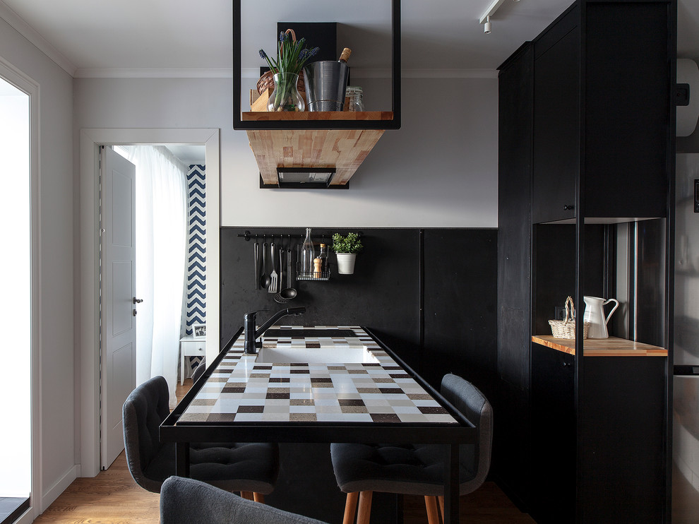 Foto på ett litet funkis kök, med en undermonterad diskho, släta luckor, svarta skåp, svart stänkskydd, mellanmörkt trägolv och en halv köksö