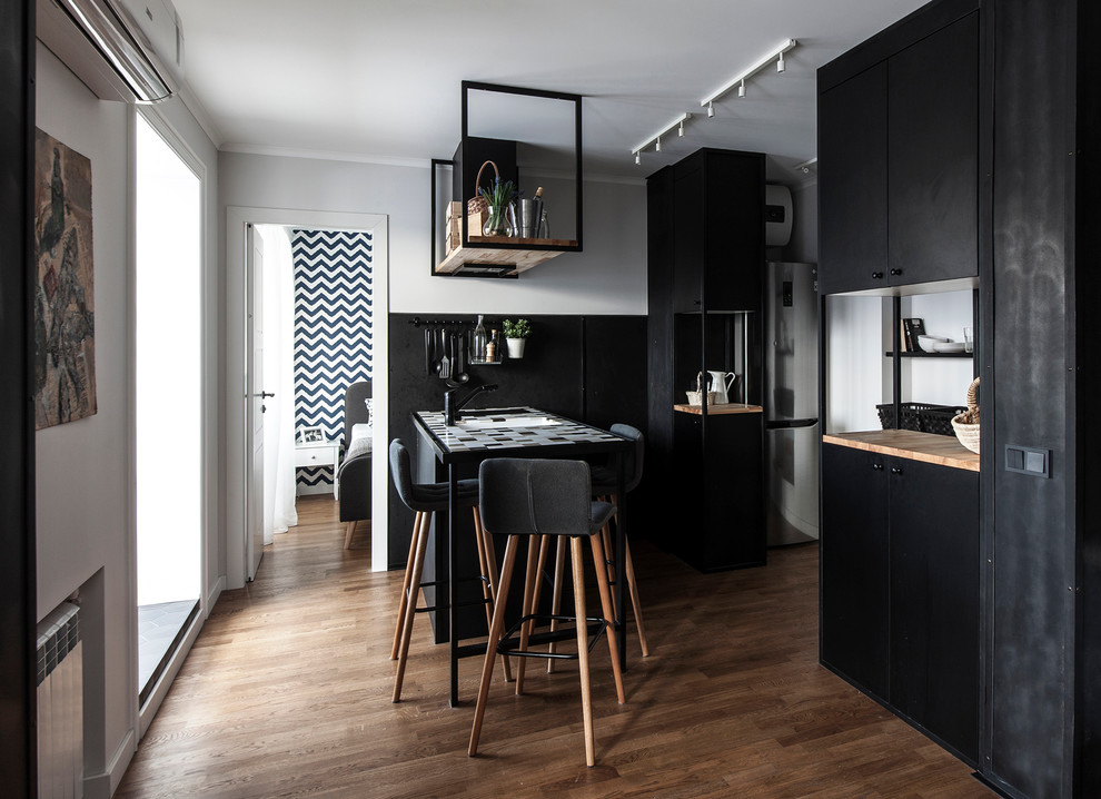 Inspiration pour une petite cuisine ouverte parallèle design avec des portes de placard noires, plan de travail carrelé, une crédence noire, un sol en bois brun, une péninsule, un sol marron et un plan de travail multicolore.