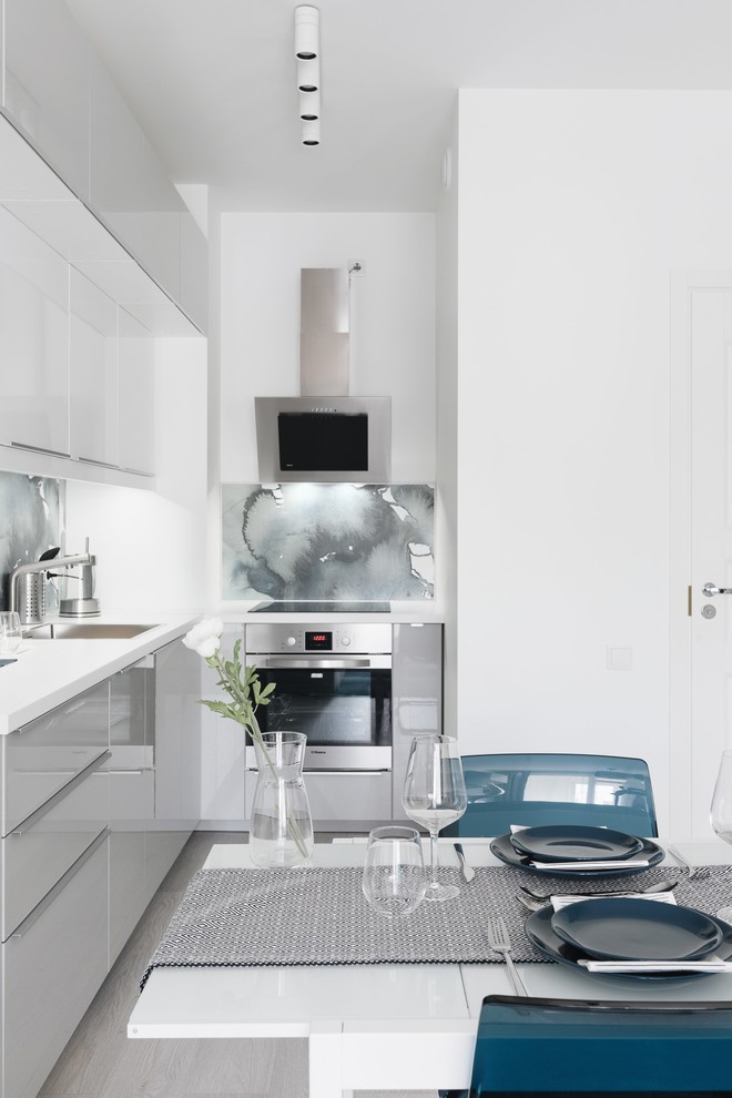 Bild på ett minimalistiskt vit vitt kök, med en nedsänkt diskho, släta luckor, grå skåp, laminatbänkskiva, blått stänkskydd, rostfria vitvaror, laminatgolv och grått golv