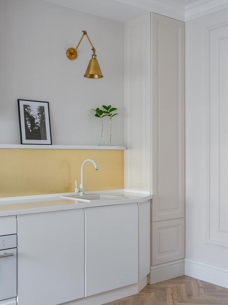 Cette image montre une cuisine linéaire design avec un évier posé, un placard à porte plane, des portes de placard blanches, une crédence jaune, un électroménager blanc, un sol marron, un plan de travail blanc et un sol en bois brun.