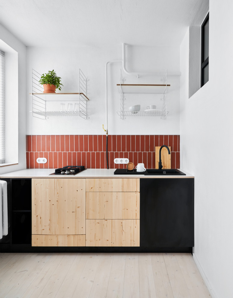 Cette image montre une cuisine design avec un évier posé, un placard à porte plane, des portes de placard noires, une crédence orange, un sol en bois brun, aucun îlot, un sol beige et un plan de travail blanc.