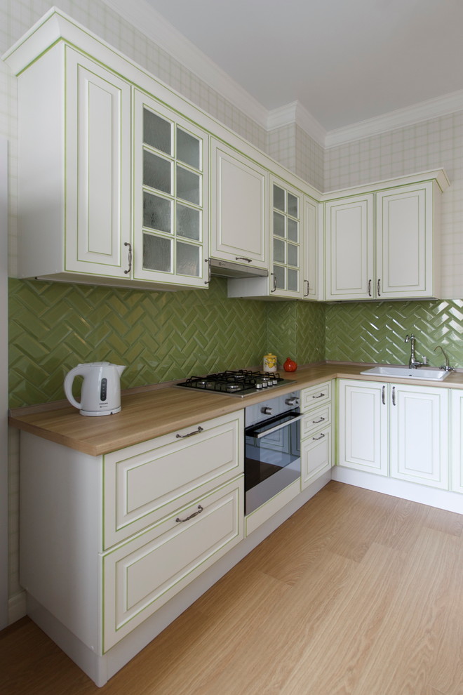 Пример оригинального дизайна: отдельная, угловая кухня в скандинавском стиле с фасадами с выступающей филенкой, белыми фасадами, зеленым фартуком, фартуком из керамической плитки, накладной мойкой и паркетным полом среднего тона без острова