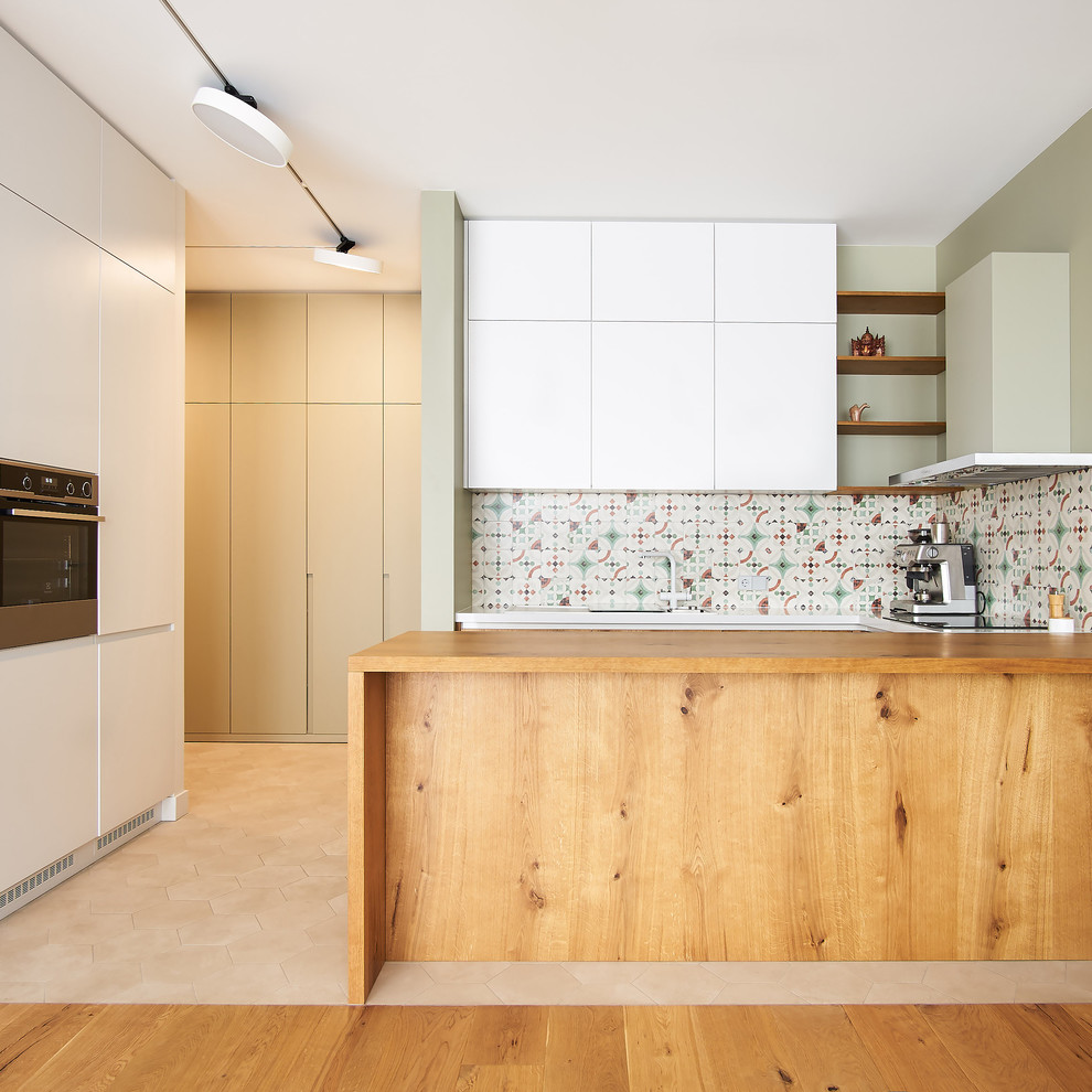 Design ideas for a contemporary u-shaped kitchen in Other with flat-panel cabinets, white cabinets, wood worktops, multi-coloured splashback, stainless steel appliances, a breakfast bar, beige floors and brown worktops.