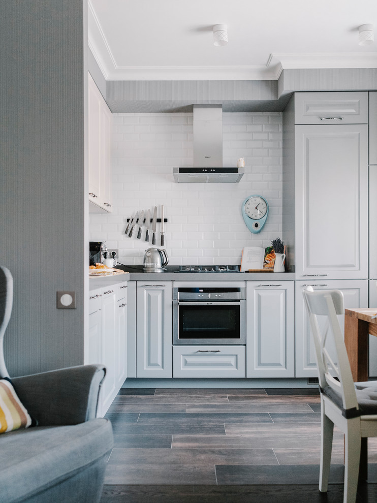 Источник вдохновения для домашнего уюта: угловая кухня-гостиная в классическом стиле с фасадами с выступающей филенкой, белыми фасадами и белым фартуком без острова