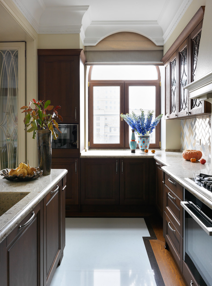 Klassisk inredning av ett mellanstort, avskilt beige beige u-kök, med en integrerad diskho, bruna skåp, bänkskiva i kvarts, flerfärgad stänkskydd, stänkskydd i keramik, svarta vitvaror, marmorgolv, en köksö, vitt golv och luckor med upphöjd panel