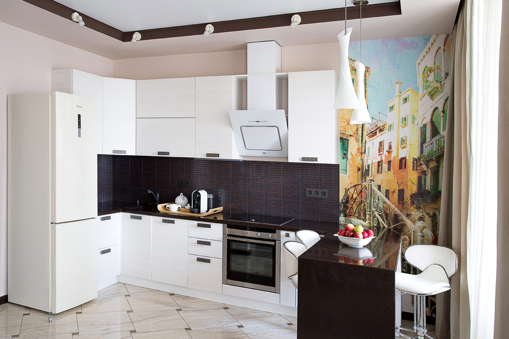 Inredning av ett modernt kök, med släta luckor, vita skåp, svart stänkskydd, rostfria vitvaror och en halv köksö