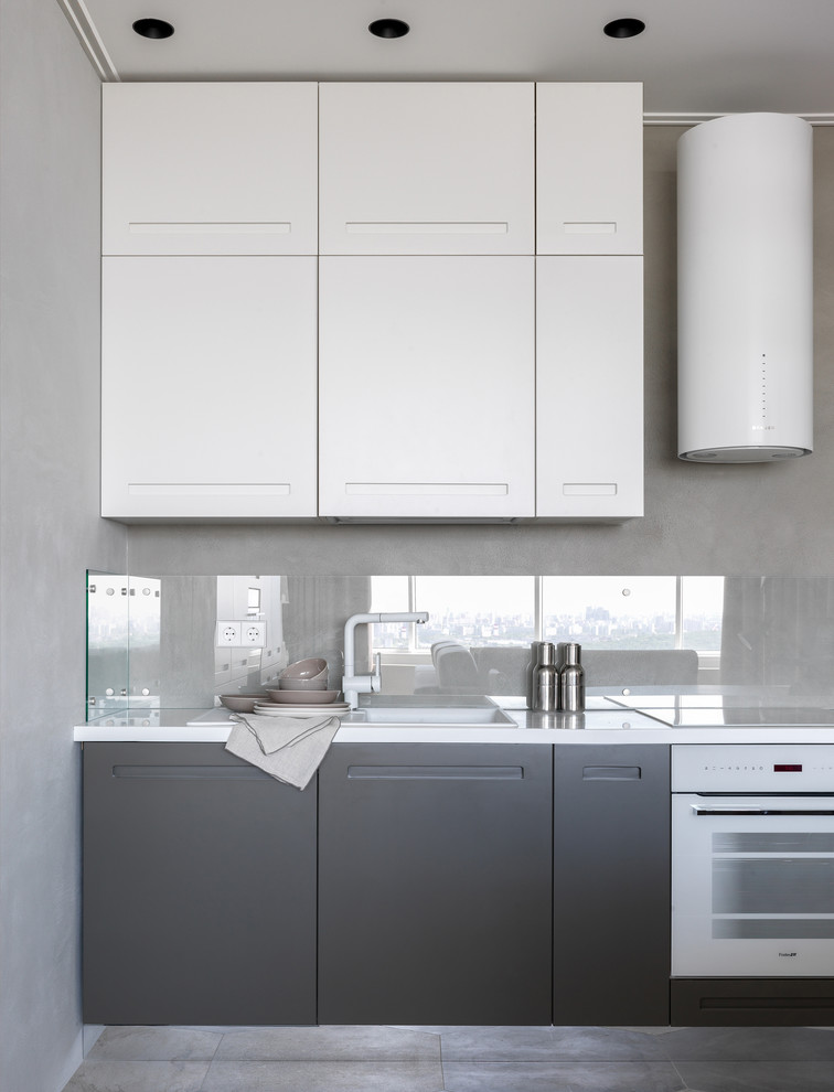 Inspiration för mellanstora moderna vitt kök, med en nedsänkt diskho, släta luckor, glaspanel som stänkskydd, vita vitvaror, klinkergolv i keramik, grå skåp, grått stänkskydd och grått golv