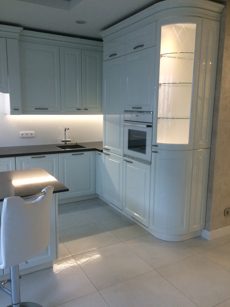 Design ideas for a medium sized traditional l-shaped kitchen/diner in Other with a submerged sink, raised-panel cabinets, white cabinets, quartz worktops, white splashback, white appliances, ceramic flooring, an island, white floors and black worktops.