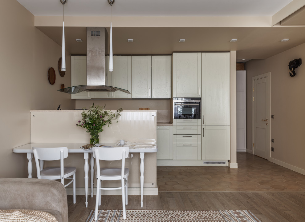 Immagine di una cucina minimal con ante in stile shaker, ante bianche, paraspruzzi beige, elettrodomestici in acciaio inossidabile, penisola e pavimento marrone