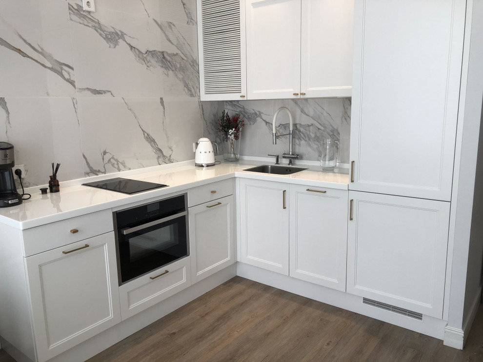 На фото: угловая кухня-гостиная в современном стиле с белыми фасадами с