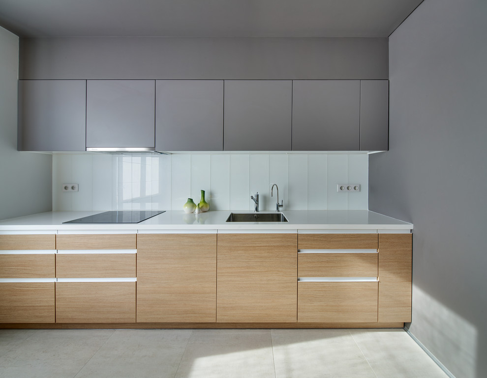 Cette photo montre une cuisine linéaire tendance avec un évier encastré, un placard à porte plane, des portes de placard grises, une crédence blanche et une crédence en carreau de verre.