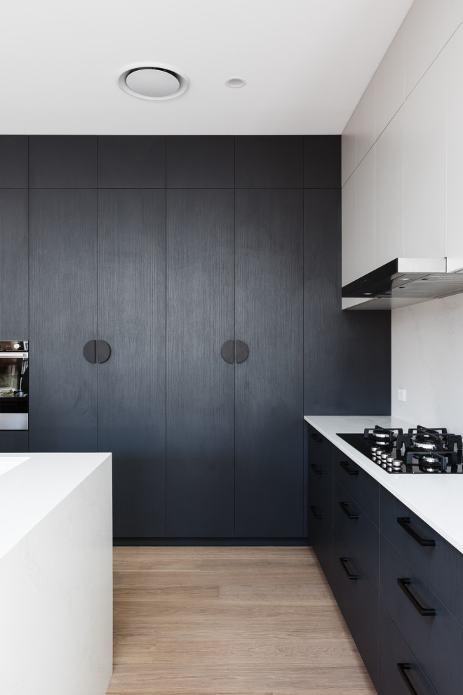 Moderne Küche mit schwarzen Schränken, Küchenrückwand in Weiß, hellem Holzboden und weißer Arbeitsplatte