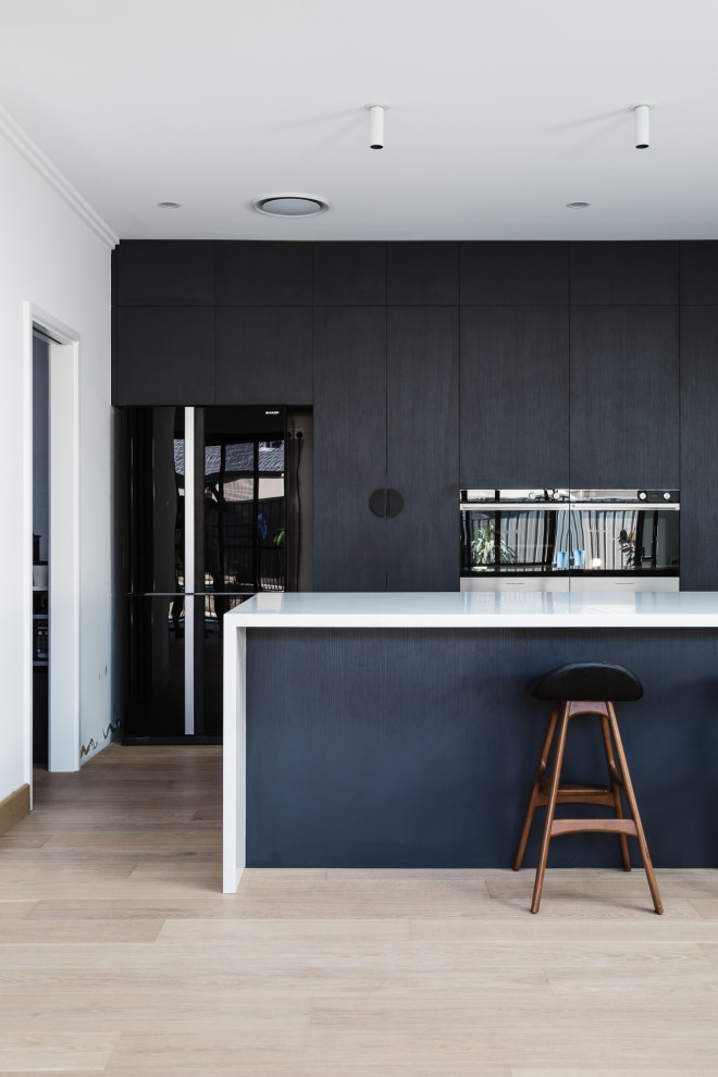 Foto di una cucina minimal con ante nere, parquet chiaro e top bianco