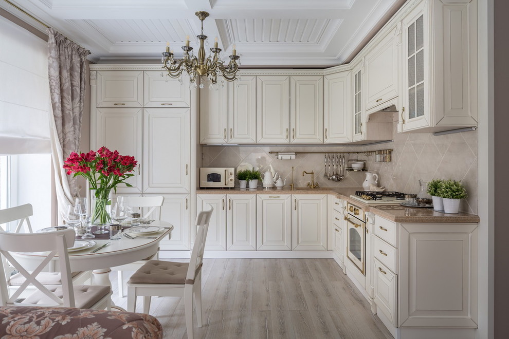 Traditional l-shaped open plan kitchen in Other with raised-panel cabinets, white cabinets, beige splashback, white appliances, light hardwood flooring, no island, beige floors and beige worktops.