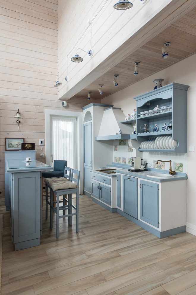 Lantlig inredning av ett linjärt kök med öppen planlösning, med blå skåp, kaklad bänkskiva, vitt stänkskydd, stänkskydd i keramik, klinkergolv i porslin, en nedsänkt diskho, luckor med infälld panel, en halv köksö och beiget golv