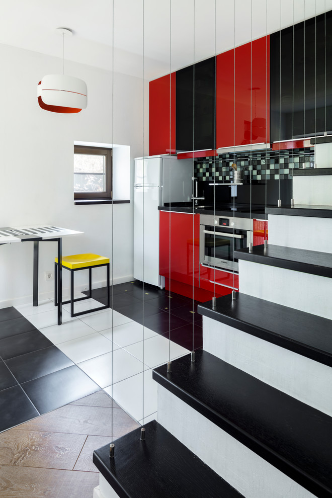 Exempel på ett litet modernt svart linjärt svart kök med öppen planlösning, med släta luckor, röda skåp, rostfria vitvaror, flerfärgat golv, flerfärgad stänkskydd och stänkskydd i mosaik