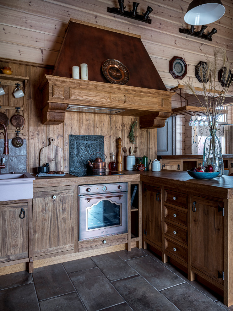 Inredning av ett lantligt brun brunt l-kök, med en rustik diskho, skåp i shakerstil, skåp i mellenmörkt trä, träbänkskiva, brunt stänkskydd, stänkskydd i trä, rostfria vitvaror, en halv köksö och grått golv