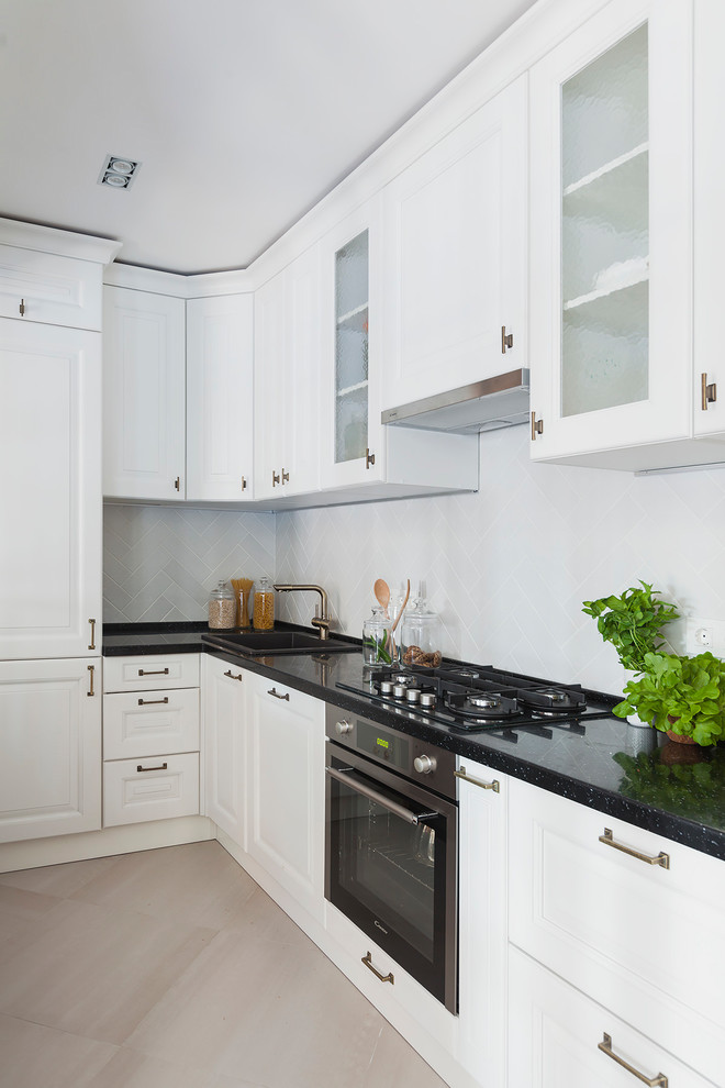 This is an example of a traditional l-shaped enclosed kitchen in Moscow with a built-in sink, white splashback, stainless steel appliances, beige floors, black worktops, raised-panel cabinets and no island.