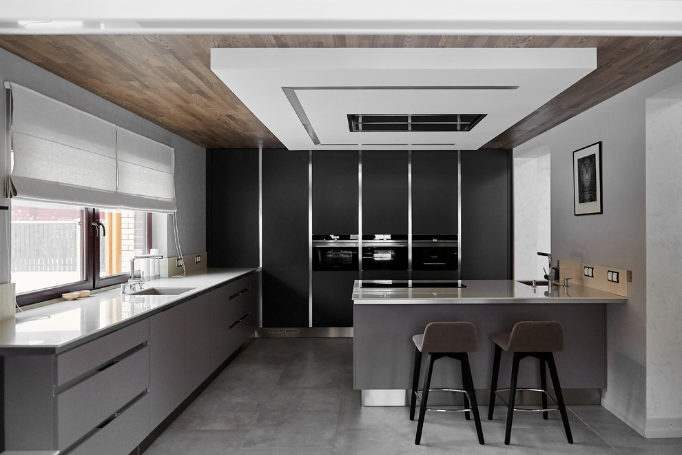 Стильный дизайн: кухня в современном стиле с врезной мойкой, плоскими фасадами, серыми фасадами, серым полом, белой столешницей, полуостровом и мойкой у окна - последний тренд