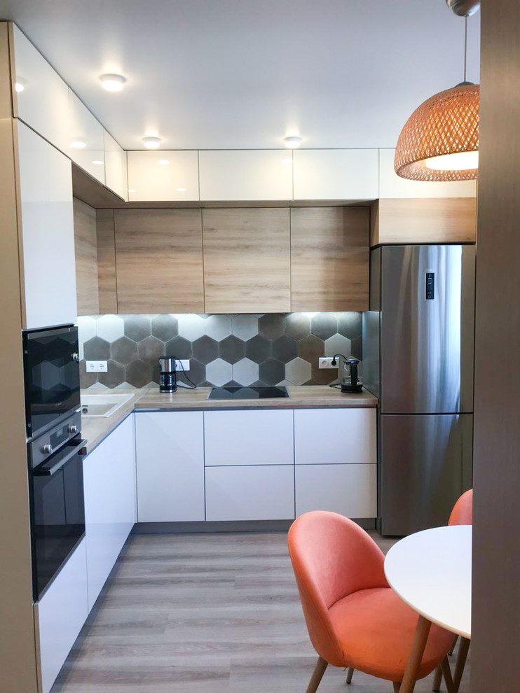 Small contemporary l-shaped enclosed kitchen in Saint Petersburg with a submerged sink, white cabinets, wood worktops, brown splashback, porcelain splashback, stainless steel appliances, laminate floors, no island, beige floors and beige worktops.