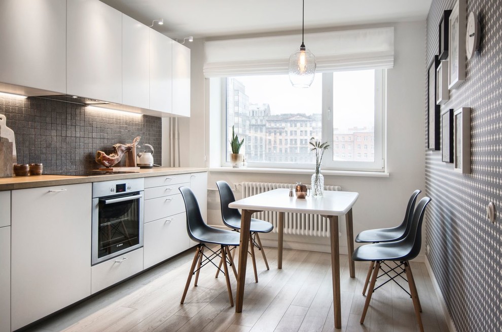 Exempel på ett litet skandinaviskt linjärt kök och matrum, med en nedsänkt diskho, släta luckor, vita skåp, träbänkskiva, stänkskydd i keramik, rostfria vitvaror, laminatgolv och grått stänkskydd