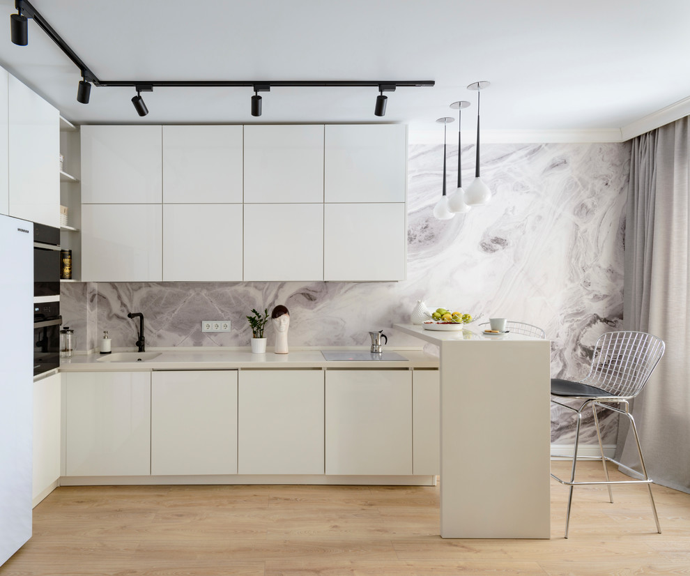 Idee per una piccola cucina a L design con ante lisce, ante bianche, paraspruzzi grigio, parquet chiaro, penisola, pavimento beige e top bianco