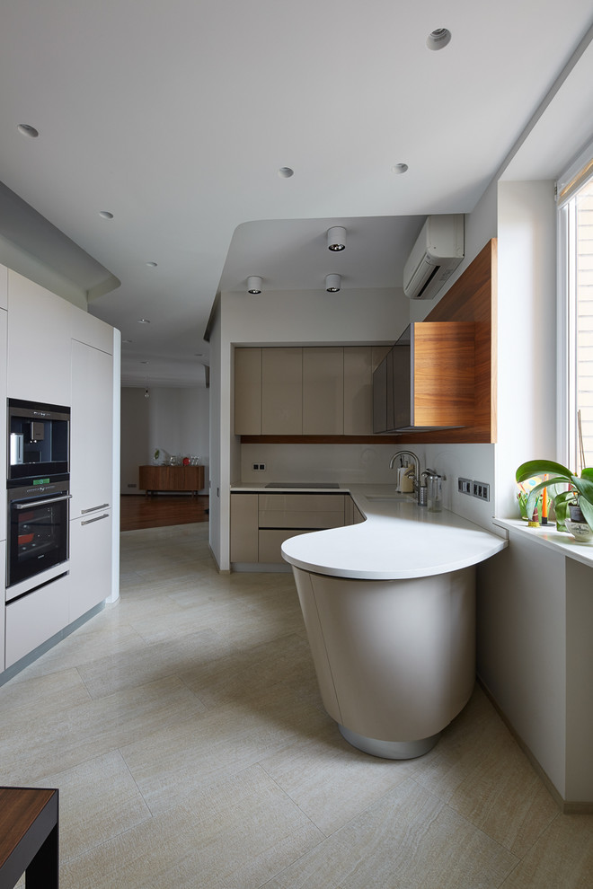 На фото: угловая кухня в современном стиле с врезной мойкой, плоскими фасадами, серыми фасадами, белым фартуком и техникой из нержавеющей стали