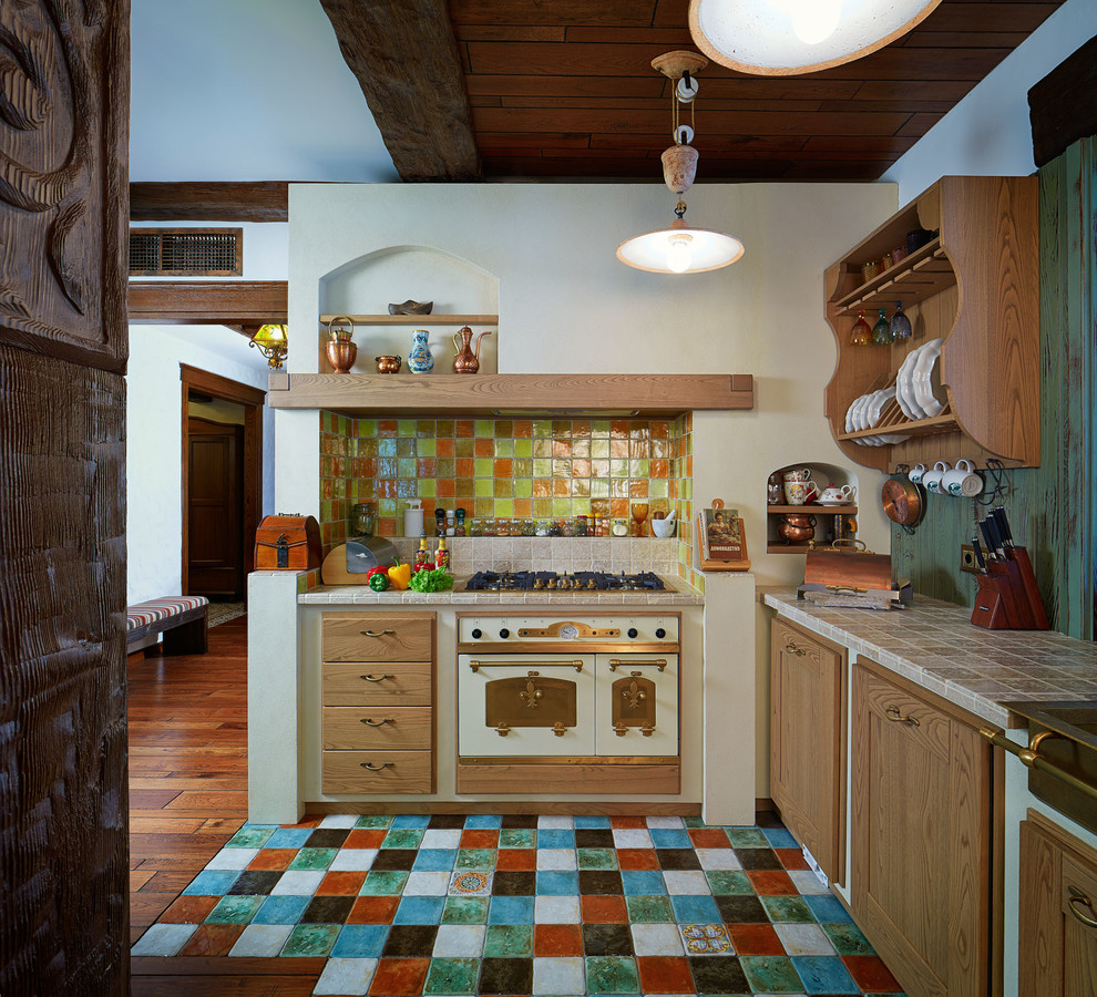 Inredning av ett lantligt l-kök, med skåp i mellenmörkt trä, flerfärgad stänkskydd, stänkskydd i terrakottakakel, klinkergolv i terrakotta, flerfärgat golv, kaklad bänkskiva och vita vitvaror