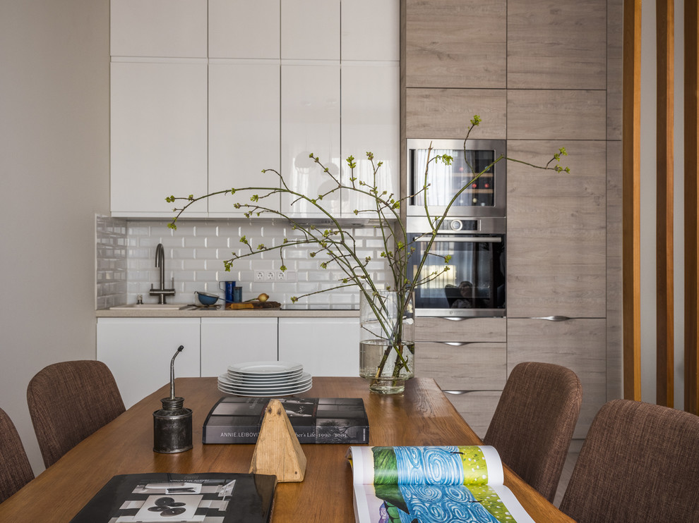 Foto de cocina comedor lineal, actual, sin isla, con fregadero encastrado, armarios con paneles lisos, salpicadero blanco, salpicadero de azulejos tipo metro, encimeras beige, puertas de armario blancas y electrodomésticos de acero inoxidable