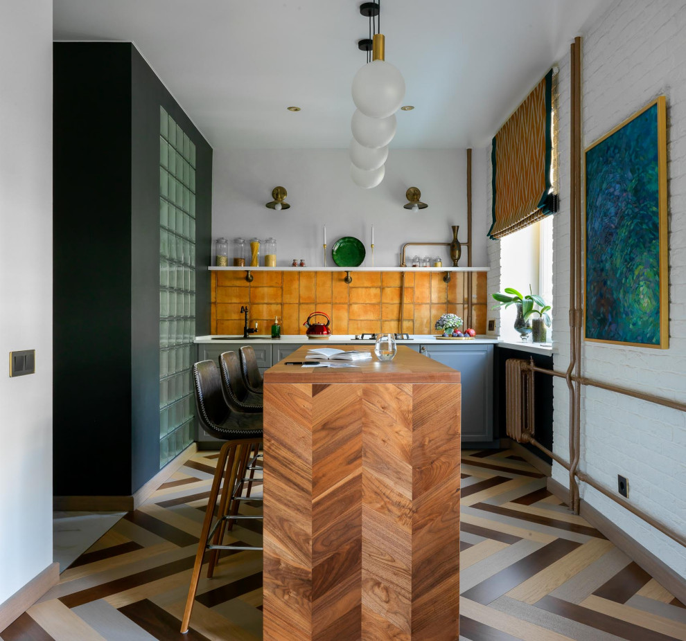 Exempel på ett litet modernt vit linjärt vitt kök med öppen planlösning, med en nedsänkt diskho, luckor med infälld panel, grå skåp, bänkskiva i koppar, orange stänkskydd, stänkskydd i keramik, svarta vitvaror, mellanmörkt trägolv, en köksö och flerfärgat golv