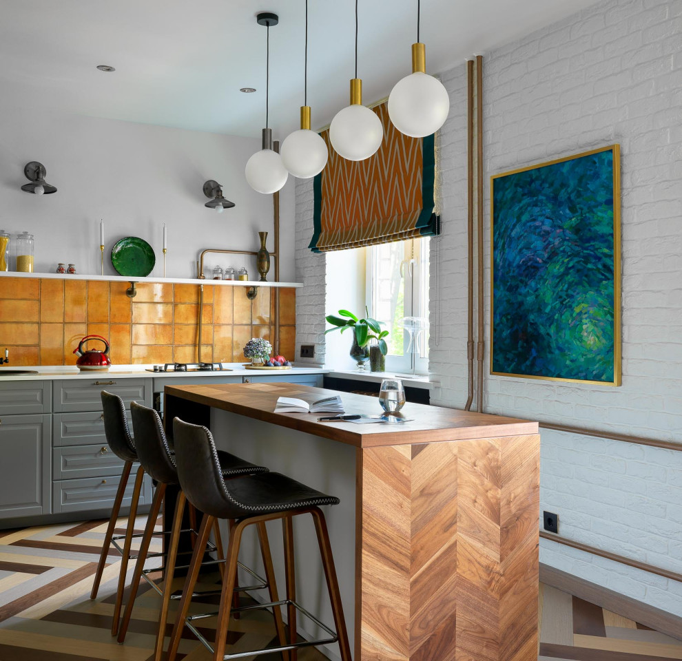 Inspiration for a small eclectic single-wall medium tone wood floor and multicolored floor open concept kitchen remodel in Moscow with a drop-in sink, recessed-panel cabinets, gray cabinets, solid surface countertops, orange backsplash, ceramic backsplash, black appliances, an island and white countertops