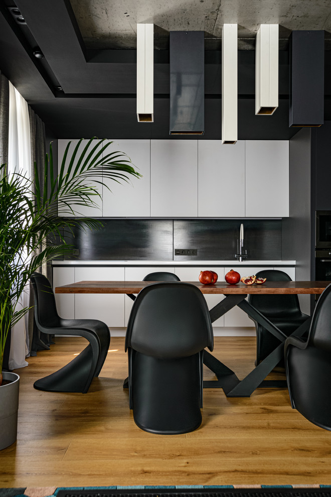Moderne Küche mit flächenbündigen Schrankfronten, weißen Schränken, Küchenrückwand in Schwarz, braunem Holzboden und weißer Arbeitsplatte in Novosibirsk