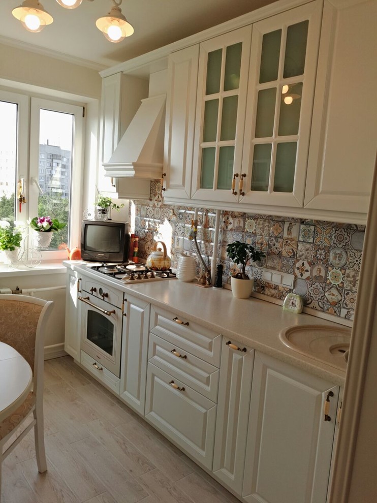 Foto på ett litet lantligt beige linjärt kök och matrum, med en nedsänkt diskho, luckor med upphöjd panel, vita skåp, laminatbänkskiva, flerfärgad stänkskydd och vita vitvaror