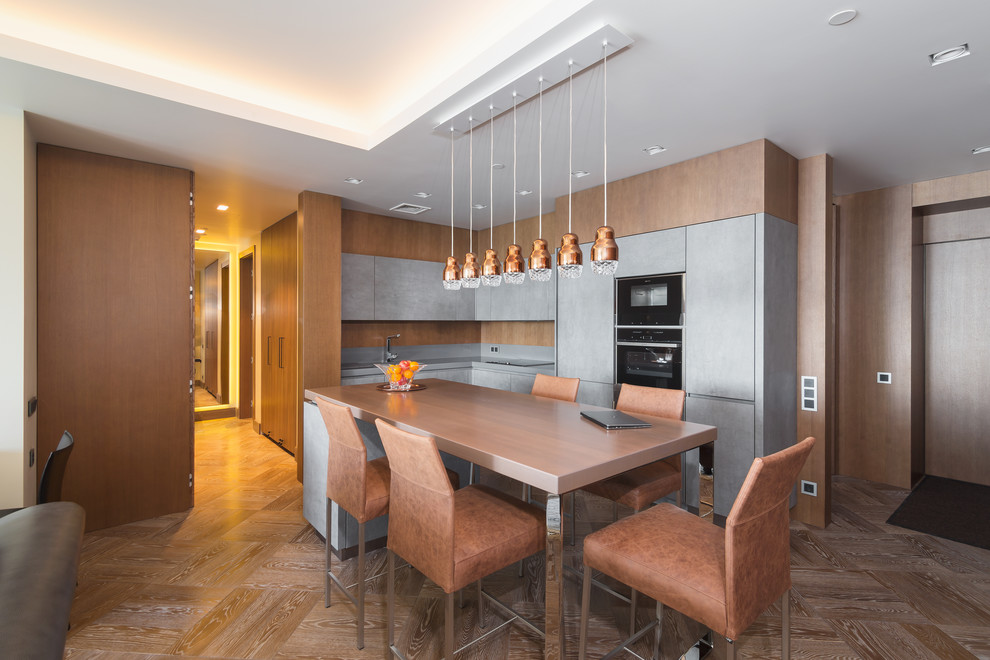 Esempio di una cucina minimal con ante lisce, ante grigie, elettrodomestici neri, pavimento in legno massello medio, pavimento marrone e top grigio
