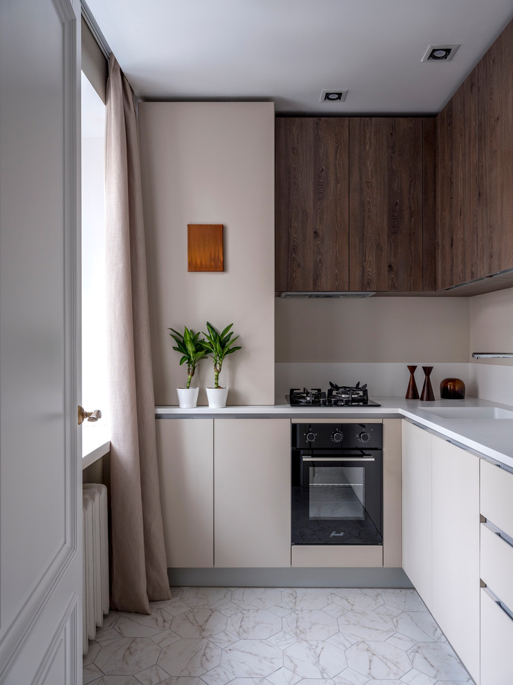 Réalisation d'une cuisine bicolore design en L avec un placard à porte plane, des portes de placard beiges, une crédence beige, un électroménager noir, un plan de travail blanc, un évier intégré et un sol blanc.
