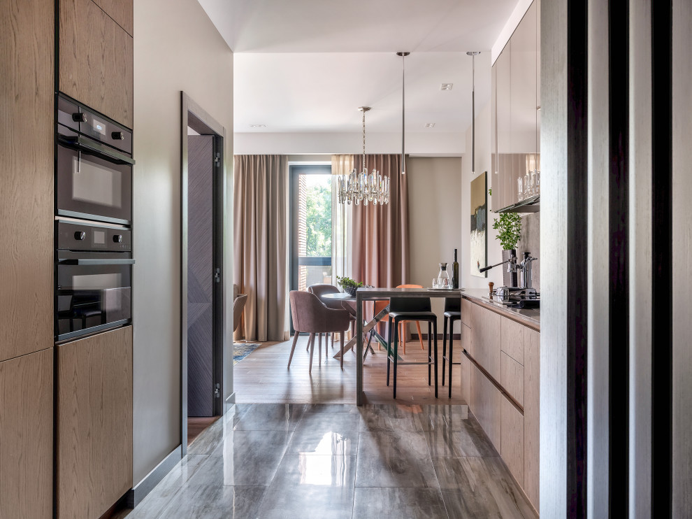 Идея дизайна: параллельная кухня-гостиная в современном стиле с плоскими фасадами, фасадами цвета дерева среднего тона и серым полом без острова