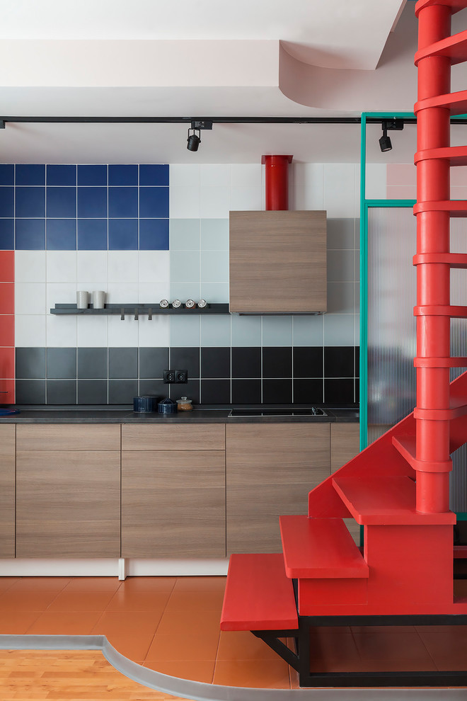 Diseño de cocina lineal moderna con armarios con paneles lisos, puertas de armario de madera oscura, salpicadero multicolor, salpicadero de azulejos de cerámica, suelo naranja y encimeras negras