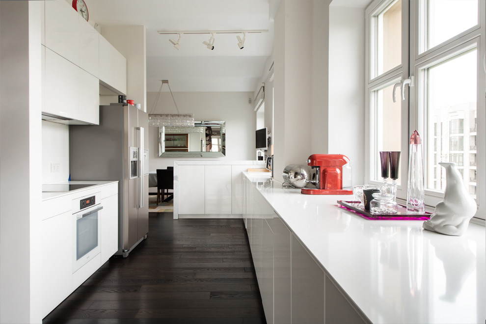 Foto di una grande cucina minimal con ante lisce, ante bianche, top in vetro, paraspruzzi bianco, elettrodomestici bianchi, parquet scuro, pavimento nero e top bianco