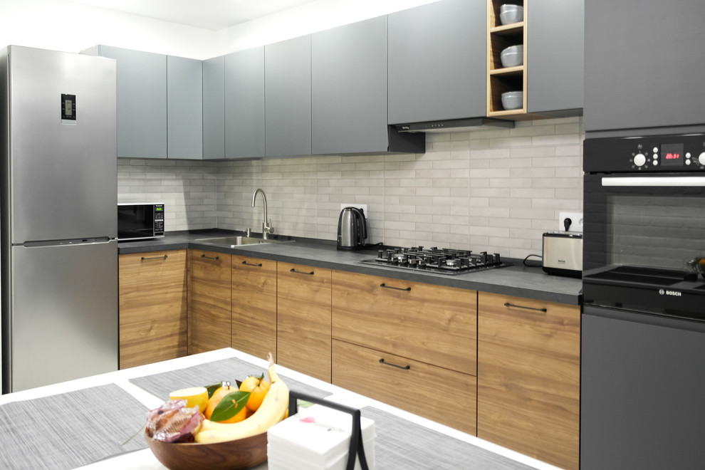 Example of a mid-sized urban l-shaped laminate floor and gray floor enclosed kitchen design in Other with gray cabinets, laminate countertops, subway tile backsplash, black appliances, no island, a single-bowl sink, flat-panel cabinets, beige backsplash and gray countertops