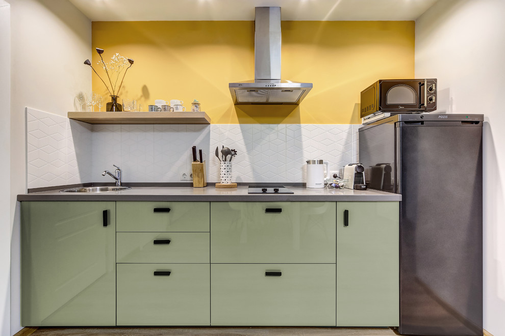 Diseño de cocina lineal actual abierta sin isla con fregadero encastrado, armarios con paneles lisos, puertas de armario verdes, salpicadero blanco, suelo laminado y encimeras grises