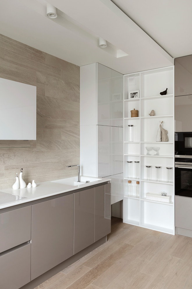 Modern inredning av ett kök, med en integrerad diskho, släta luckor, beige stänkskydd, svarta vitvaror, ljust trägolv och beiget golv