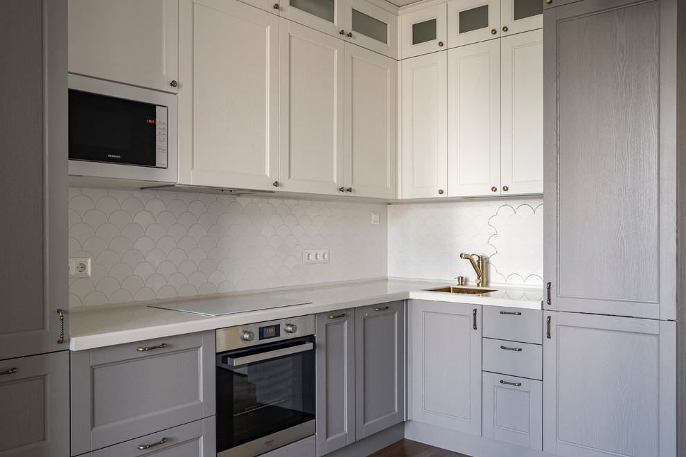Inredning av ett klassiskt avskilt vit vitt l-kök, med en undermonterad diskho, luckor med infälld panel, grå skåp, vitt stänkskydd och rostfria vitvaror