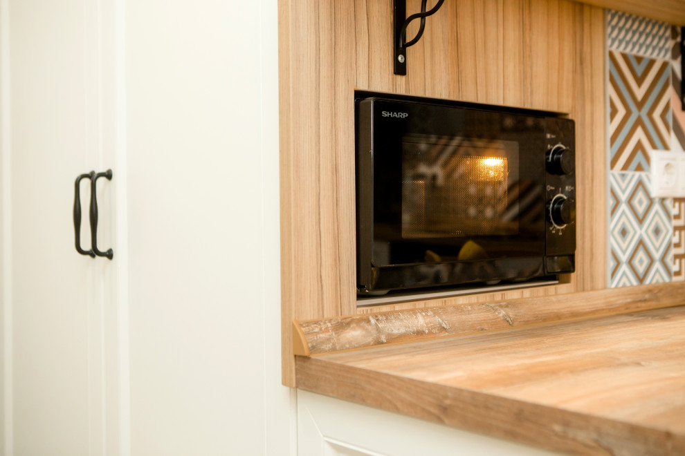 Cette photo montre une petite cuisine américaine scandinave en L avec un placard avec porte à panneau encastré, un plan de travail en bois, une crédence en céramique et un électroménager noir.