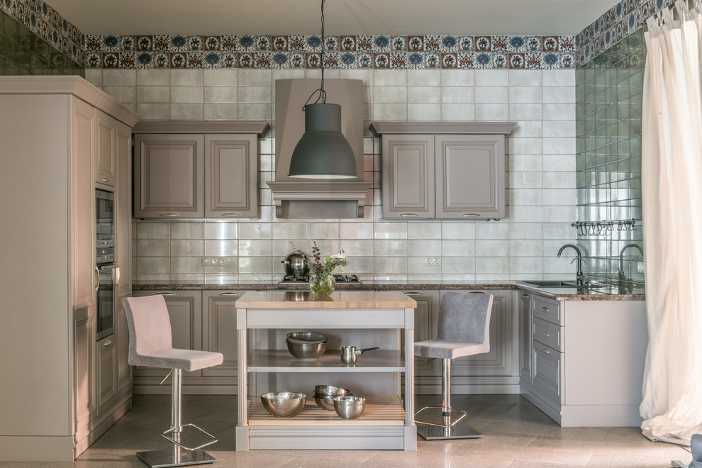 Moderne Küche in L-Form mit Einbauwaschbecken, profilierten Schrankfronten, grauen Schränken, Küchenrückwand in Grau, Rückwand aus Spiegelfliesen, Küchengeräten aus Edelstahl, Kücheninsel, beigem Boden und brauner Arbeitsplatte in Sonstige