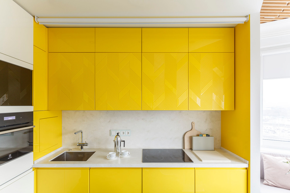 Пример оригинального дизайна: отдельная, угловая кухня в современном стиле с врезной мойкой, плоскими фасадами, желтыми фасадами, белым фартуком и черной техникой без острова