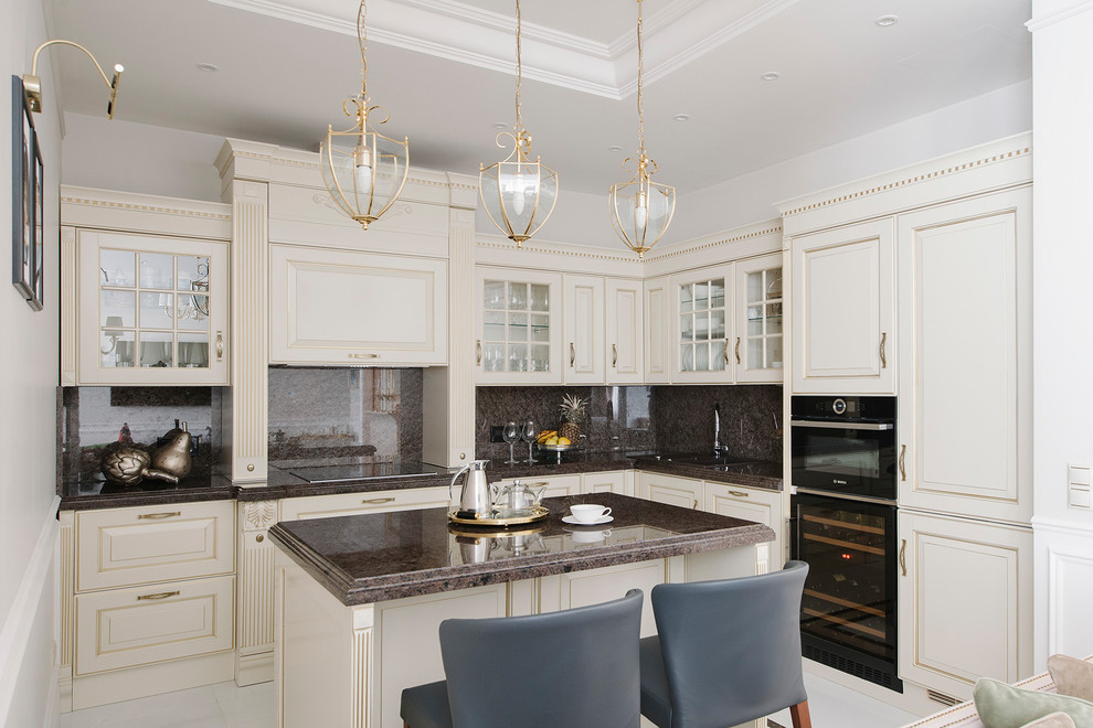 Пример оригинального дизайна: угловая, светлая кухня-гостиная в классическом стиле с одинарной мойкой, стеклянными фасадами, бежевыми фасадами, коричневым фартуком, черной техникой, островом и коричневой столешницей