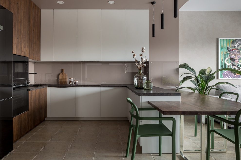 Photo of a small contemporary u-shaped open plan kitchen in Other with flat-panel cabinets, white cabinets, laminate countertops, black appliances, porcelain flooring, a breakfast bar, black worktops, a submerged sink, grey splashback, glass sheet splashback and grey floors.