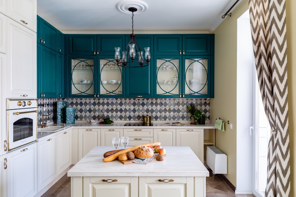 Exemple d'une cuisine bicolore chic en L avec un évier posé, un placard à porte vitrée, des portes de placard turquoises, une crédence multicolore, un électroménager blanc, îlot, un sol marron et un plan de travail blanc.