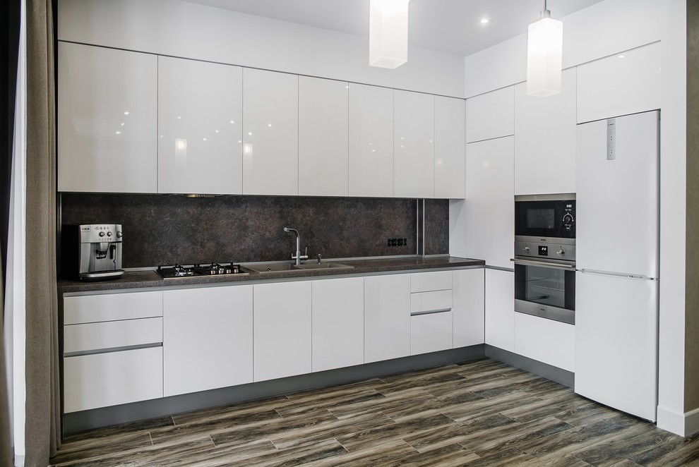 This is an example of a medium sized contemporary l-shaped open plan kitchen in Other with flat-panel cabinets, white cabinets, stainless steel appliances, ceramic flooring, no island, brown floors, a double-bowl sink, grey splashback and grey worktops.